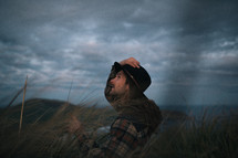 a man in a plaid shirt and hat standing under cloudy skies in New Zealand 