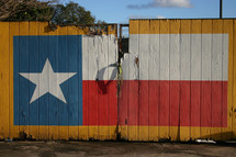 A Texas flag painted on a yellow fence