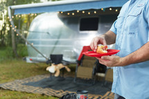 a man carrying a hotdog on a plate in front of a camper 