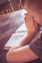 boy child with praying hands over the pages of a Bible 