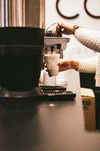 A woman getting a cup of coffee from a coffee machine.