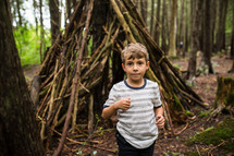 boy and a teepee of sticks in the woods 