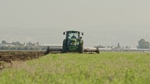 Tractor cultivating a green field in slow motion.