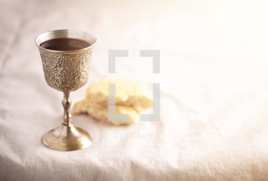 Unleavened bread, chalice of wine, silver kiddush wine cup on canvas background. Communion still life. Christian communion concept for reminder of Jesus sacrifice. Easter passover.