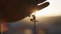Hands clasp rosary at sunset