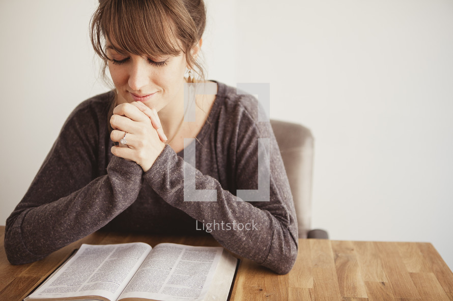 woman with her hands folded in prayer over a Bible