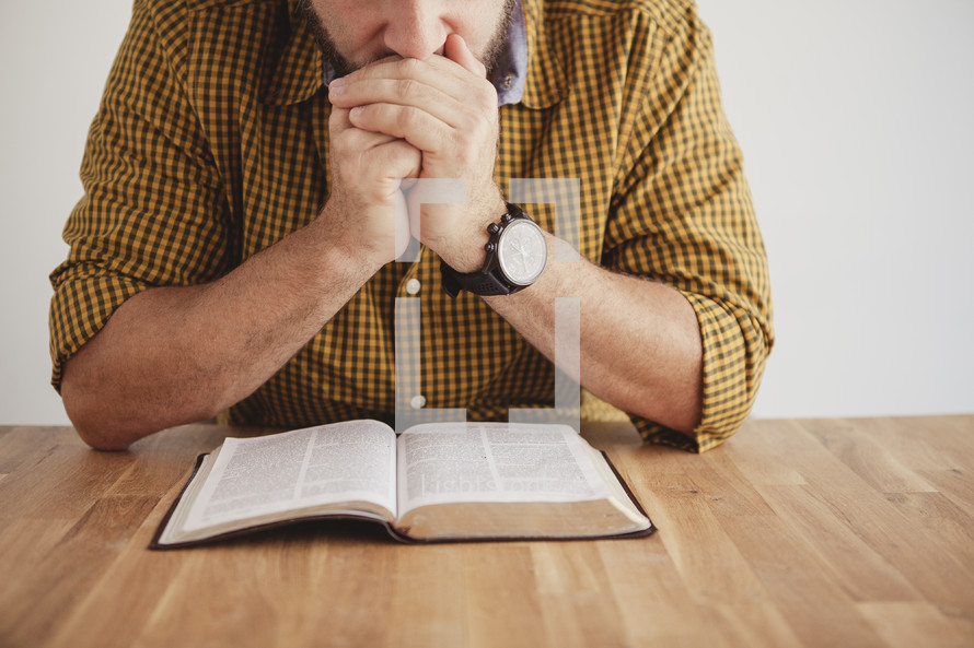 man reading a Bible with his hands folded in prayer