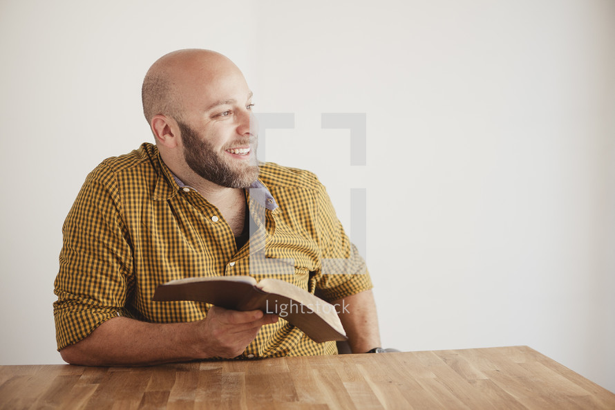 man smiling to the side reflecting while reading a Bible