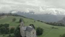 Aerial shot of beautiful gothic church with green hills and mountains in background 