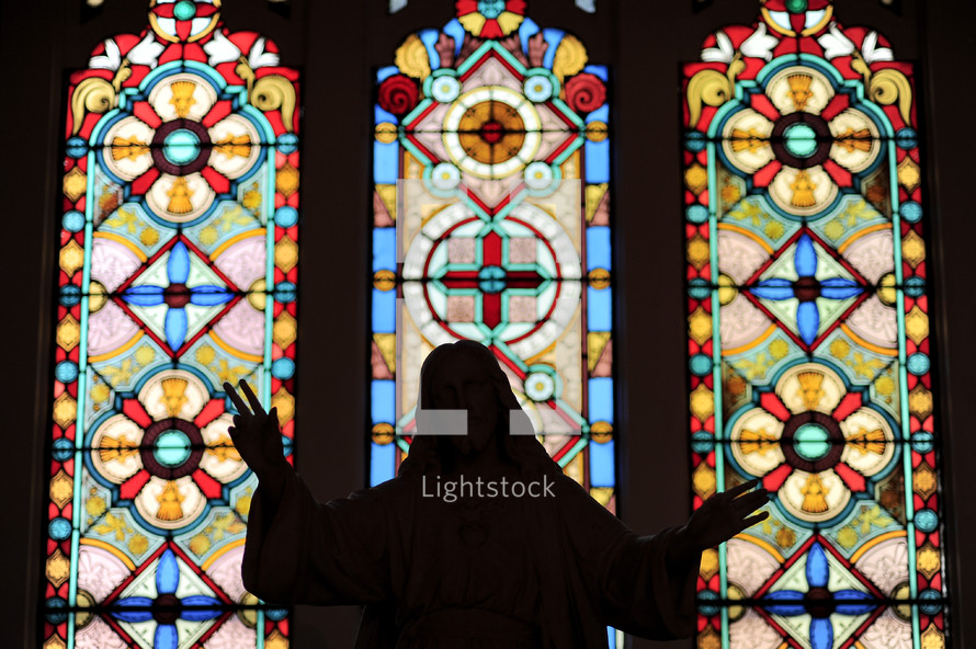 silhouette of a statue of Jesus in front of stained glass windows