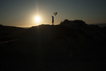 Girl with balloons on ridge at sunset
