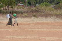 women carrying buckets down a dirt road