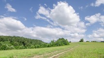 Clouds sky over green countryside with gravel road in sunny summer nature Time lapse
