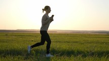 Young fitness sport woman running on road at sunset. Young woman runs in summer in park and listens to music with headphones. The concept of a healthy lifestyle.