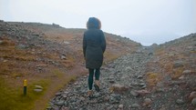 a woman in a coat walking up a gravel path 