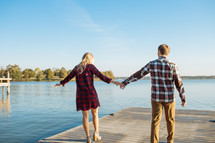 a couple holding hands walking on a dock 