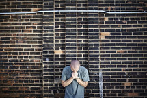 A man praying against a brick wall