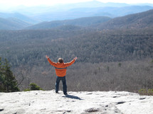 a man standing on a mountain top with raised hands 