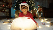 child amazed by magic book under Christmas tree