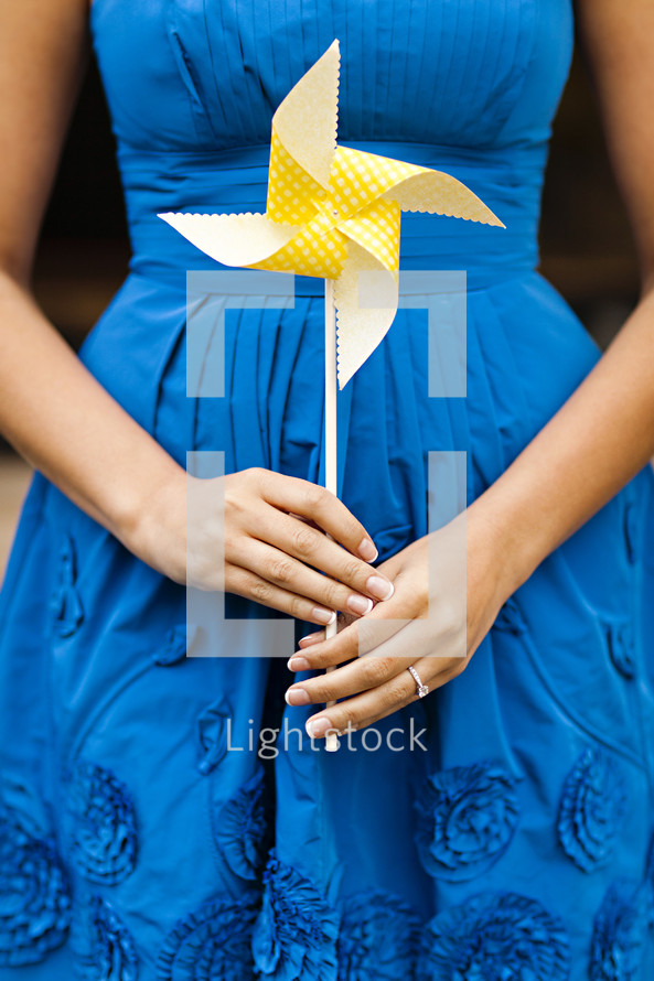 A woman in a blue dress holding a yellow whirligig pinwheel 