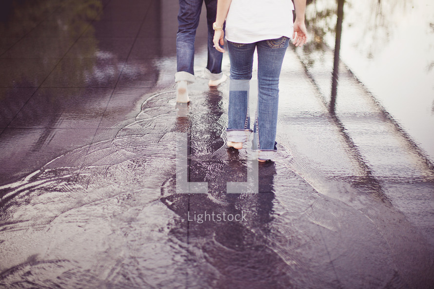People walking barefoot through puddles on the sidewalk
