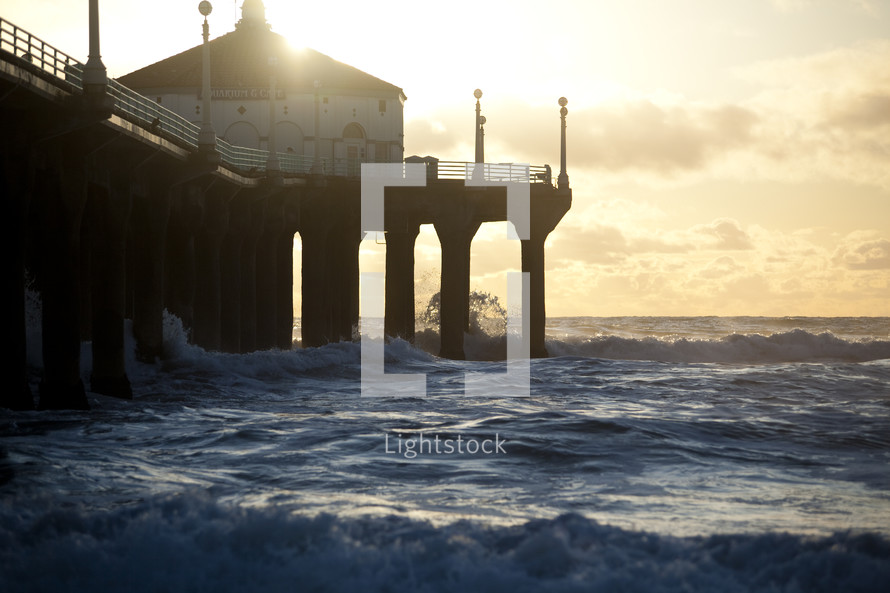 Church on a pier with waves crashing beneath it at sunset.