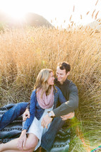 Happy Couple, man woman, sitting on blanket in field of gold tall wheat, embrace, love, romance, smile, engagement, marriage 