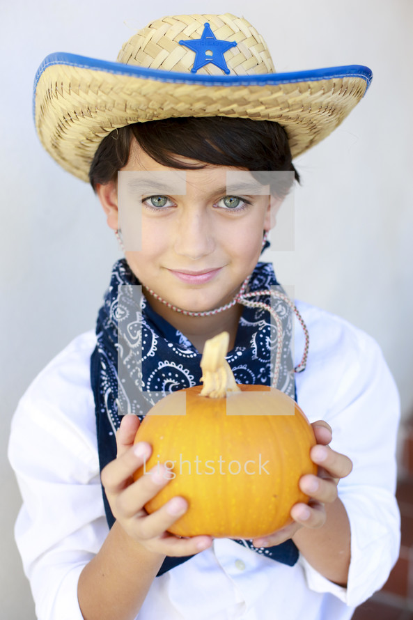 boy in a cowboy costume holding a pumpkin