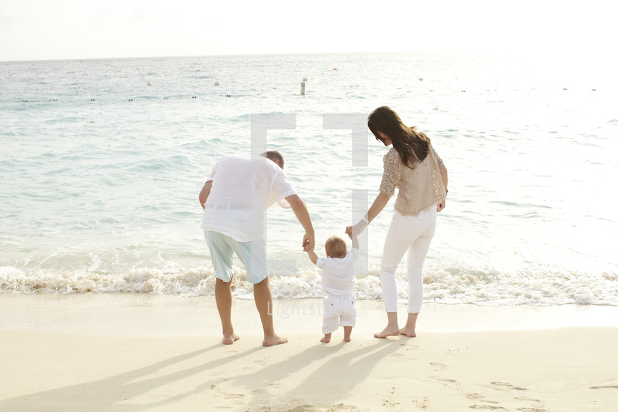 A young family stands on the beach at the edge of the ocean.  
