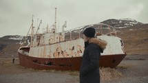 a woman walking next to a rusty ship 