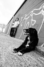 teens standing against a graffitied wall and a dog