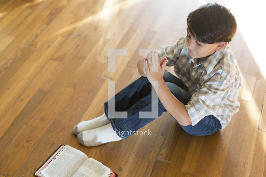 boy sitting on the floor with hands held in prayer
