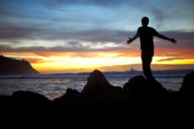 Man on beach at sunset with outstretched arms