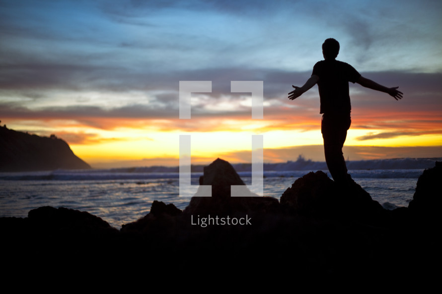 Man on beach at sunset with outstretched arms
