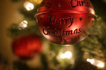 Red metal Christmas ornament with Merry Christmas hanging on Christmas tree.