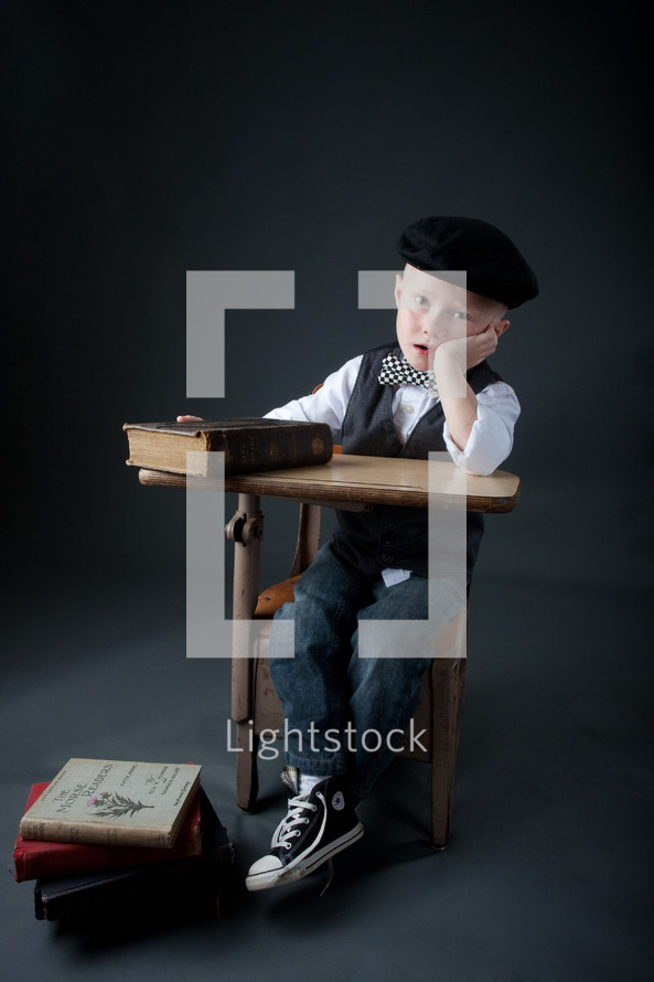 boy child sitting at a desk with his head on his hand in front of a stack of books