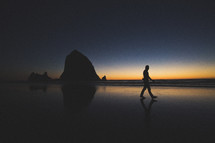 silhouette of a man walking on a beach at dusk