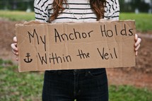 Woman holding a sign with the words MY ANCHOR HOLDS WITHIN THE VEIL 