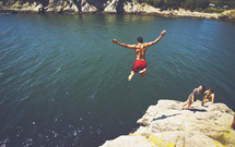 Male jumping off rock cliff into lake