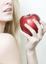 Woman (Eve) holding a red apple near her face.