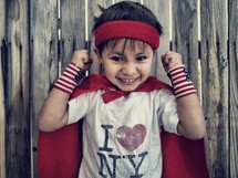 An excited boy wearing a cape and "I Heart NY" shirt