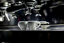 Two coffee cups under an espresso machine