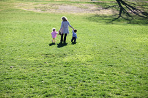 A mother holding hands and walking with her children in a field of grass.