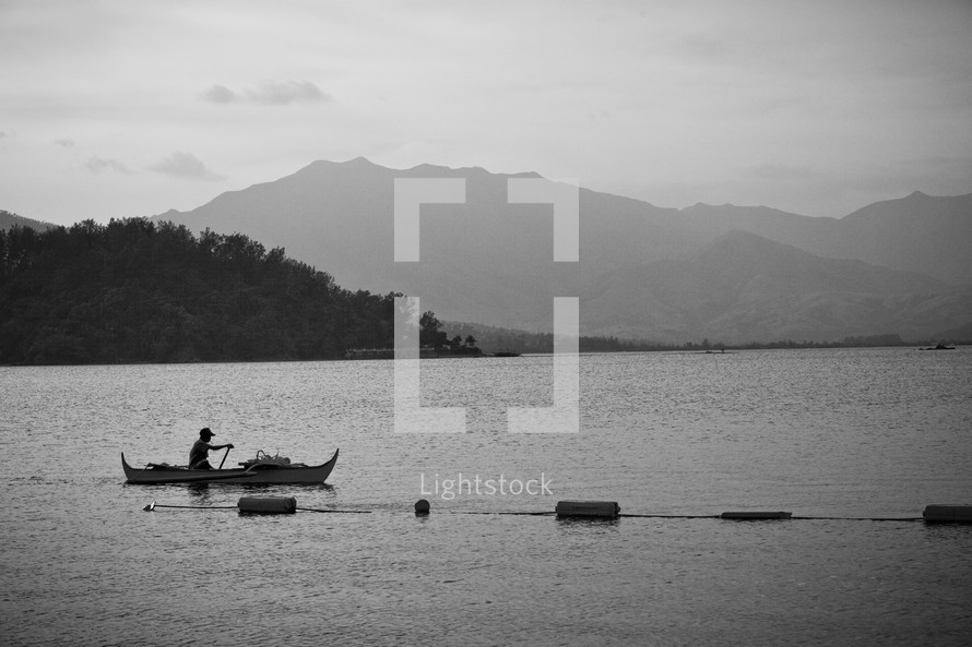 Man canoeing on open lake with mountain backdrop 