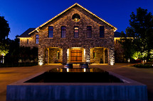 lighted stone building with wooden doors  sunset blue hour reflection fountain water night winery