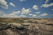 white puffy clouds over rocky ground