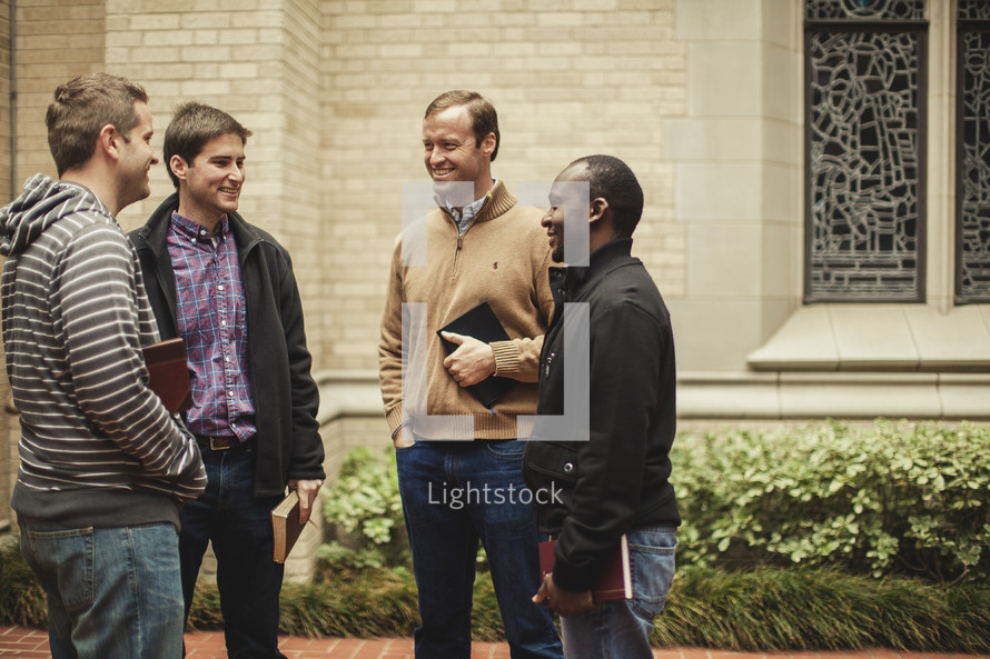 four men standing in front of a church holding Bibles