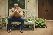 man with head bowed in prayer on a bench