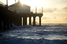 Church on a pier with waves crashing beneath it at sunset.