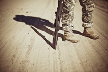A soldier standing on a dirt road with a rifle.